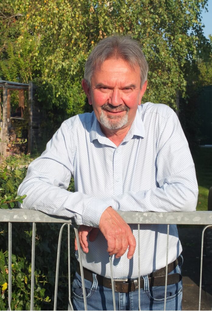 Claus Fiedler im Garten mit blauem Hemd und Zaun im Hintergrund