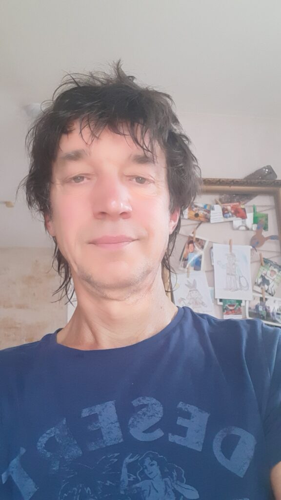 Christian Mackel lächelt in einem informellen Raum mit Pinnwand im Hintergrund