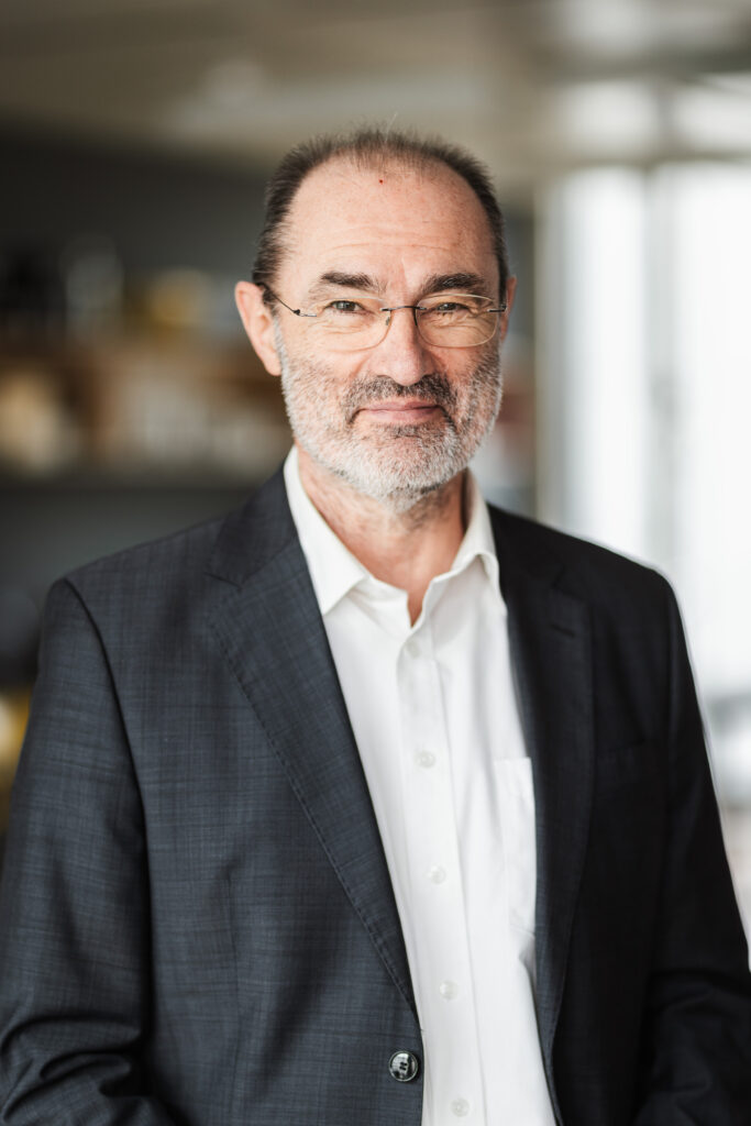 Stefan Riphaus in formeller Kleidung lächelt in die Kamera im Büro