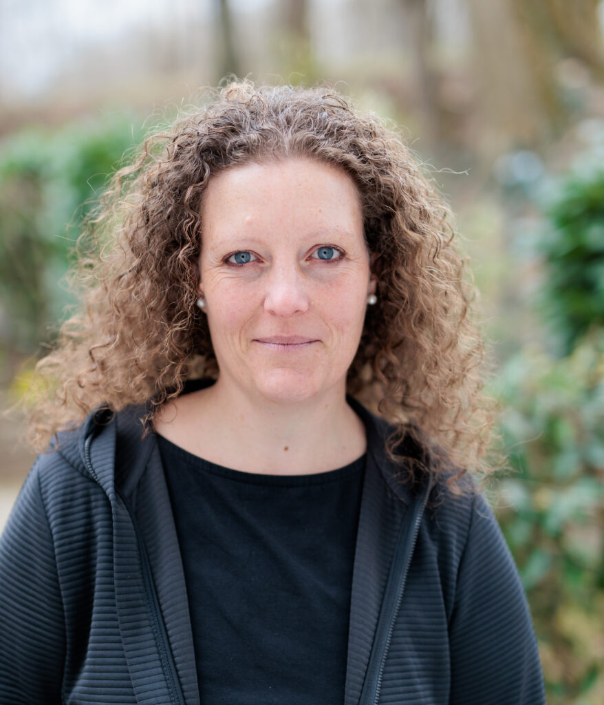 Tanja Victoria Wiedemer mit lockigem Haar steht draußen vor verschwommenem Hintergrund