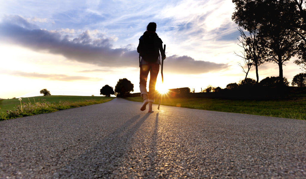 Pilgerin auf einer Landstraße im Sonnenuntergang